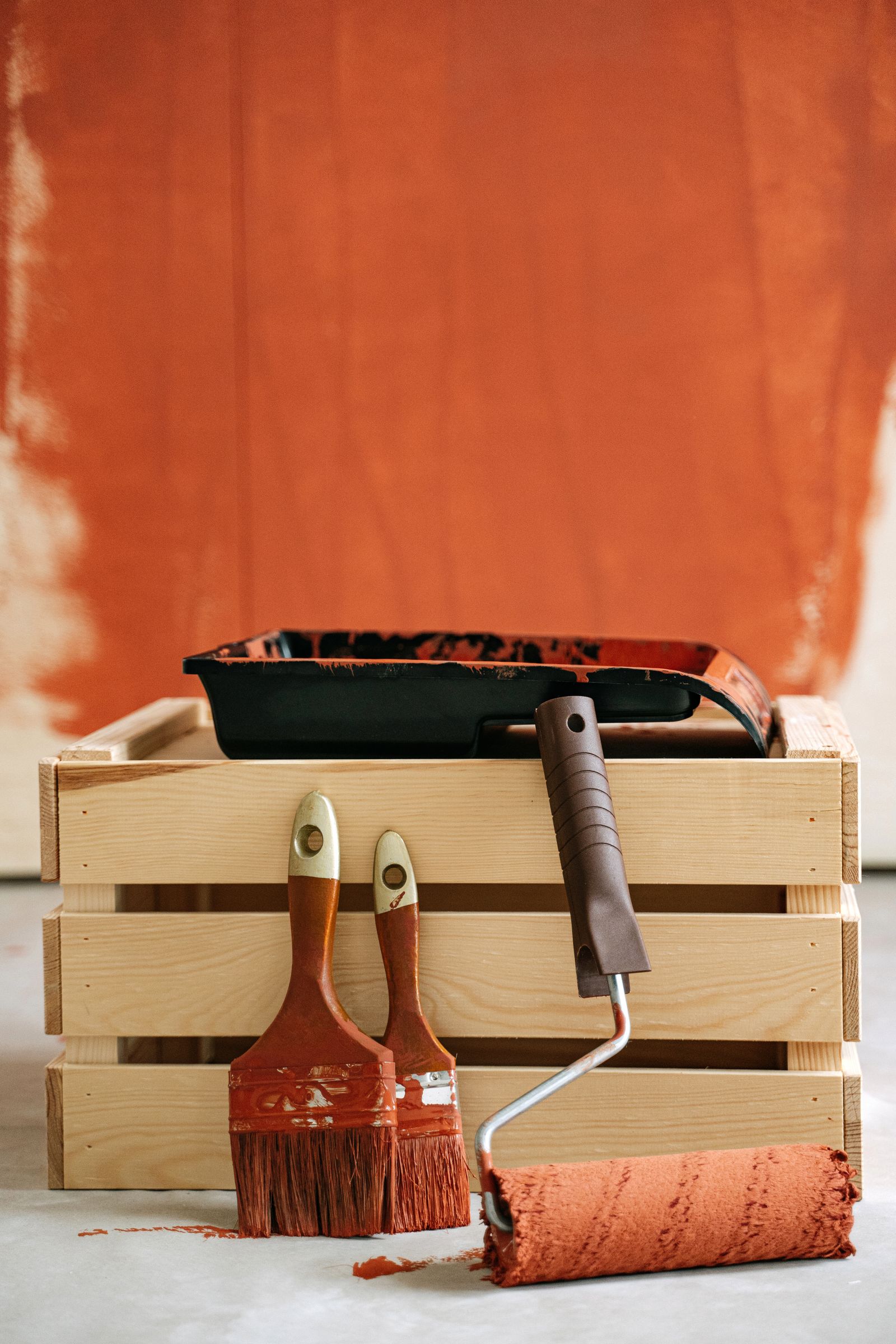 Paint tray on a wooden crate beside a roller and brushes